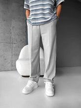 Model wearing men's light grey baggy joggers with white sneakers and striped tee in minimalist room